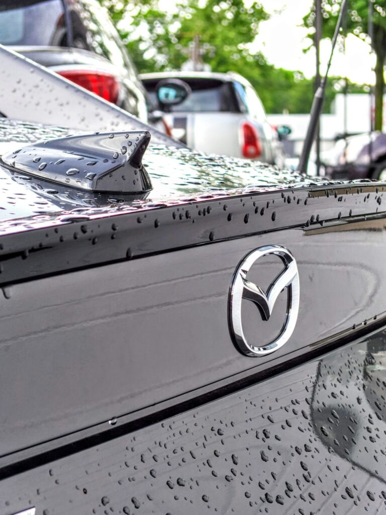 Gray Mazda Miata rear end and emblem covered in water droplets just after the rain.